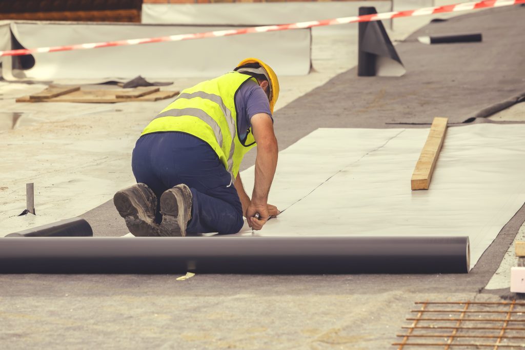 Person wearing safety vest doing construction on the floor and cutting a sheets or mat.