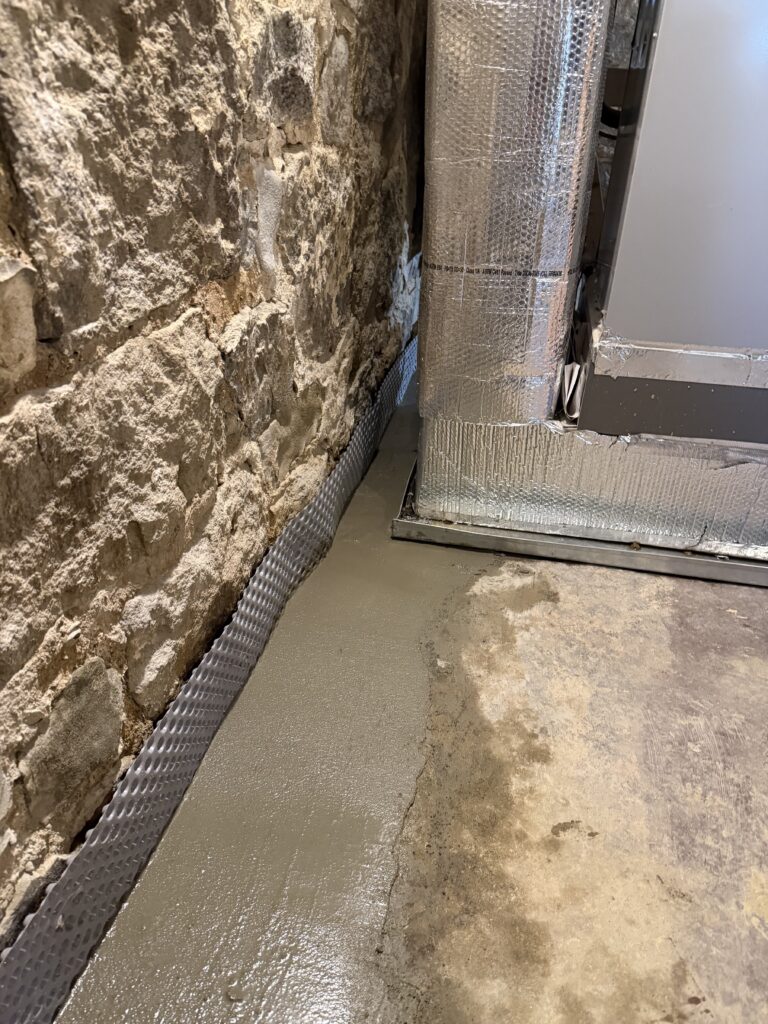Completed B-Dry interior French drain installed neatly behind basement furnace equipment
