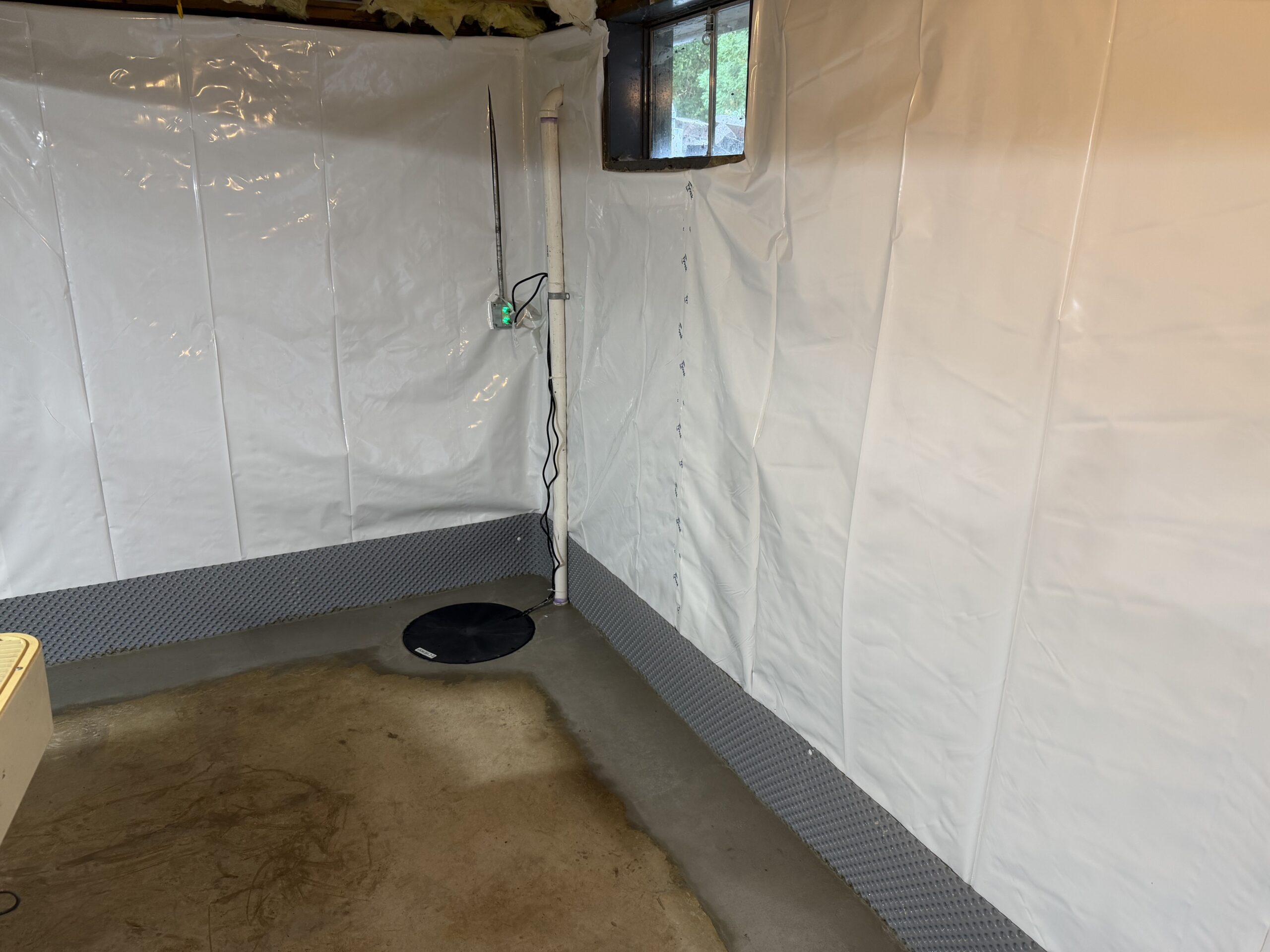 Completed basement waterproofing installation with covered sump well