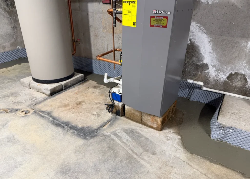 Finished interior French drain system routed around a basement water heater and furnace